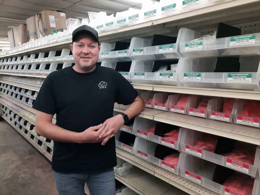 Bok Steynberg in front of shelves of glow in the dark powders